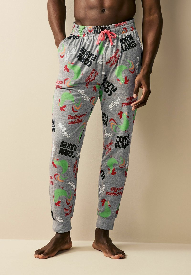 Gray pajama pants featuring a colorful print of roosters and text related to "Corn Flakes" in black and red. Elastic waistband with pink drawstring.