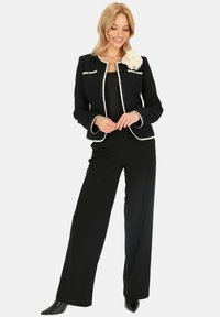 Czarna marynarka z tweedu z białymi wykończeniami i dwiema przednimi kieszeniami, z kremowym dodatkiem w kształcie kwiatu. Połączona z czarnymi spodniami o szerokich nogawkach i szpilkami.