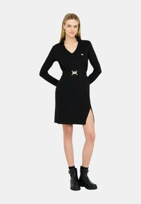 Abito nero a maniche lunghe con scollo a V e spacco laterale, dotato di una vita cintrata con una cintina dorata. Tessuto liscio, design aderente.