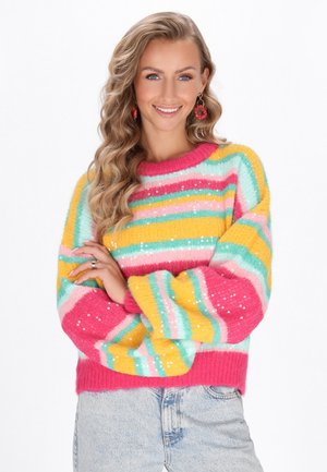 Gestreepte trui in roze, geel, blauw en groen met pailletten; heeft een ronde hals en wijde mouwen, gecombineerd met lichte spijkerbroeken.