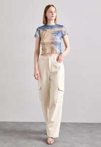 Rövid ujjú, cropped top kék és bézs absztrakt mintával; világos krémszínű, magas derekú cargo nadrággal párosítva, oldalsó zsebekkel.
