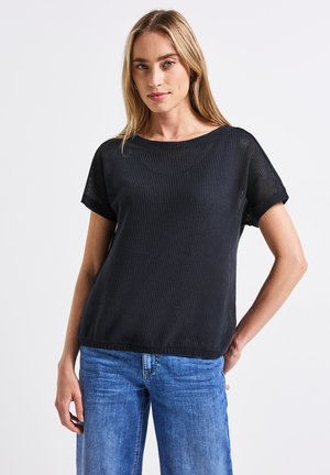 Haut noir à manches courtes avec un design texturé à tissage ouvert. Encolure arrondie et coupe décontractée, associé à un jean en denim bleu clair.