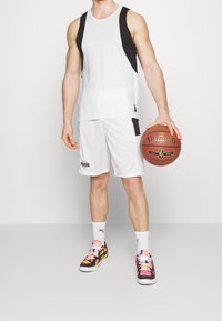 Camiseta sin mangas blanca con detalles negros, pantalones cortos blancos y zapatillas multicolores. Sosteniendo un balón de baloncesto Spalding. Diseño sencillo y ajuste atlético.