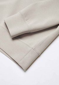Felpa grigia chiara con una texture liscia, polsini a costine e orlo piatto con dettagli di cucitura discreti.