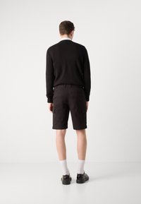 Svart strikkegenser, khaki cargo shorts med klaffelommer, hvite sokker og svarte sko. Antrekket har en avslappet passform og strømlinjeformet design.