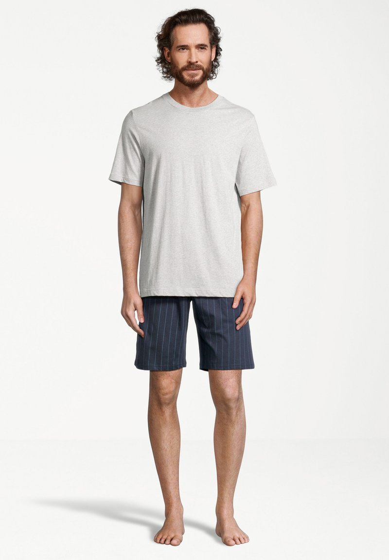 Grå bomulds t-shirt med rund halsudskæring, parret med knælange marineblå shorts med lodrette hvide striber. Model står barfodet.