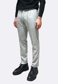 Pantaloni sartoriali grigio chiaro con pieghe, vita con coulisse e tasche laterali, abbinati a stivali neri stringati. Trama liscia.