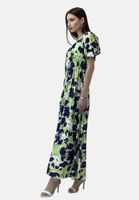 Maxikleid in Grün mit navyblumenmuster, featuring Puffärmel und gerafftem Oberteil.getragen mit weißen Riemchenheels.