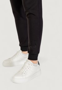 Czarne dresy z prążkowanymi mankietami i małym detalem z logo, w połączeniu z białymi skórzanymi sneakersami z czarnym akcentem na pięcie.