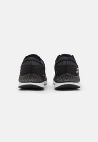 Chaussures de sport noires avec une tige en mesh et un col rembourré, dotées d'un talon texturé et d'une semelle blanche contrastante.