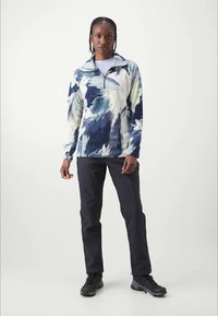 Pullover in blauw en wit abstrakt patroon, kwart-rits kraag, fleece materiaal, met zwarte broek en donkere schoenen. Gladde textuur.