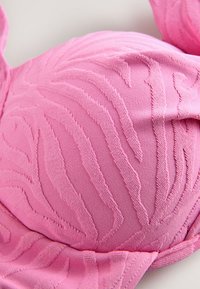 Rozā krūšturis ar faktūru riboto dizainu, gludu virsmu un izliekām kausiņām. Lentiņas un apakšējais jostu var regulēt piemērotībai.