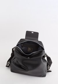 Schwarzer Leder-Rucksack mit teilweise geöffnetem Hauptfach, das eine Innentasche mit Reißverschluss und Riemenbefestigungen auf weißem Hintergrund zeigt.