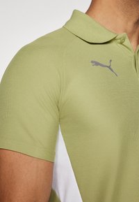 Lys grøn polo-shirt med struktureret stof, der har et sølvfarvet Puma-logo på brystet og kontrasterende hvide sidepaneler.