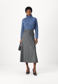 Maglione a collo alto blu a coste abbinato a una gonna lunga a trapezio grigia con dettagli di bottoni, indossato con scarpe col tacco nere.