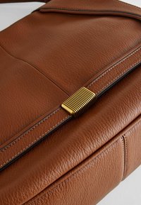 Sac à main en cuir marron avec une surface texturée, doté d'un fermoir en or strié et d'accents de couture contrastants le long des bords.