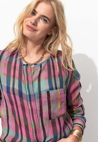 Chemise à carreaux multicolore en tissu léger, avec un col dégagé, des manches longues, une poche et un bouton de fermeture.