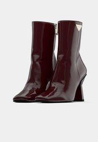 Bottines en cuir verni bordeaux avec un bout pointu, finition brillante, fermeture éclair sur le côté et un talon bloc carré. Accent en argent sur le talon.