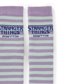 Calzini a righe viola e menta con i loghi "Stranger Things" e "Benetton" in blu. Morbido materiale lavorato a maglia con polsini a coste.