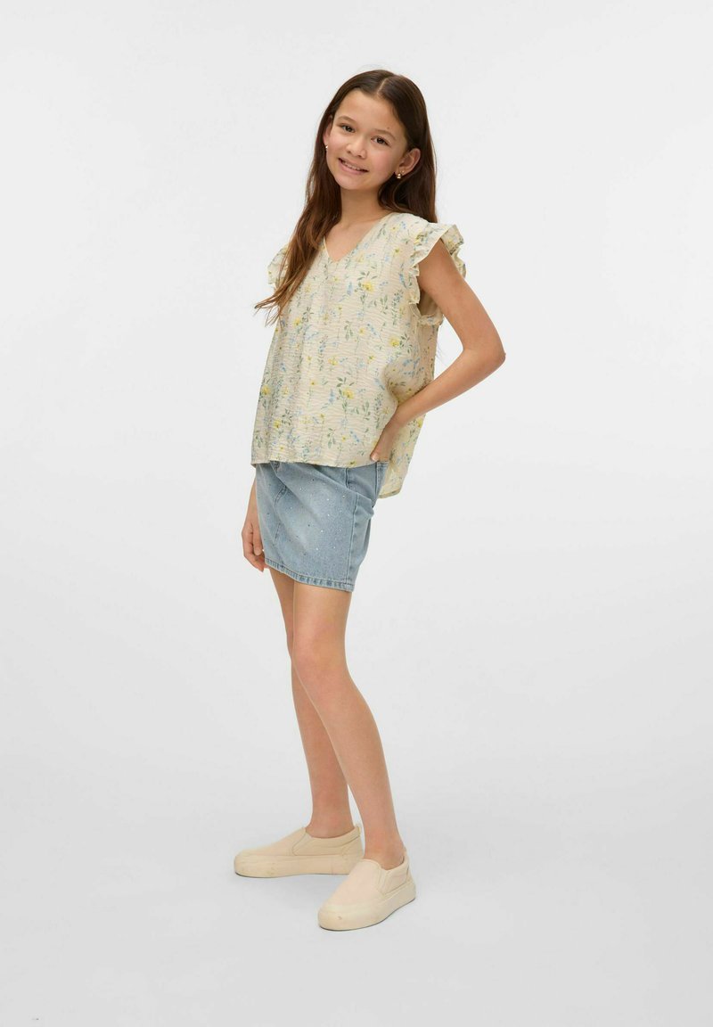 Top crema a fantasia floreale chiara con maniche a volant, abbinato a una gonna di jeans e scarpe beige senza lacci.
