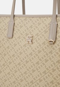 Borsa tote beige con motivo intrecciato e accenti di pelle. Presenta un logo dorato e cuciture lungo i bordi. Doppi manici per spalla.