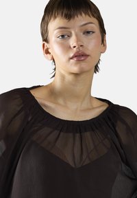 Czarna przezroczysta bluzka z szerokim dekoltem, teksturowanym materiałem i bufkami, prezentująca warstwowy fason z gładką podszewką.