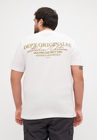 Camiseta blanca de manga corta con texto impreso en varios colores en la parte trasera, con un corte relajado y una textura de algodón suave.