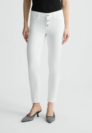 White denim jeans feature a high waist with a five-button closure, classic five-pocket design, and slim fit, paired with black and white patterned heels.