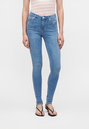 Kvinde iført lyseblå skinny jeans, en hvid og lyserød stribet ærmeløs top samt sorte sandaler med hæl og stropper.
