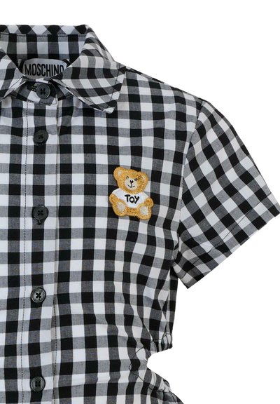 Camicia a quadretti bianco e nero con colletto, maniche corte e chiusura con bottoni frontale, con una patch di un orsetto ricamato.