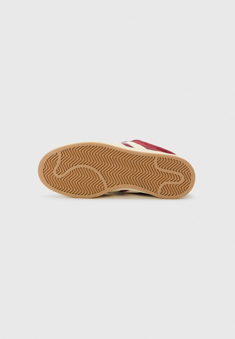 Botte de sport en suède rouge avec une semelle en caoutchouc beige dotée d'un motif en chevrons. Le design comprend des accents blancs sur le côté.