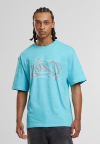 Šviesiai mėlynas medvilninis t-shirt su apvalia kaklo iškirpte ir trumpomis rankovėmis, priekyje turi sidabrinį grafikos logotipą su žvaigždėmis.