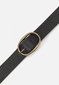 Svart läderbälte med en oval mässingsspänne. Bältet har en strukturerad finish och flera justerbara hål längs sin längd.