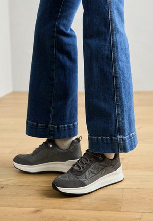 Sneaker grigi con texture e suola bianca, caratterizzati da un motivo geometrico e chiusura con lacci, abbinati a jeans a gamba larga blu.