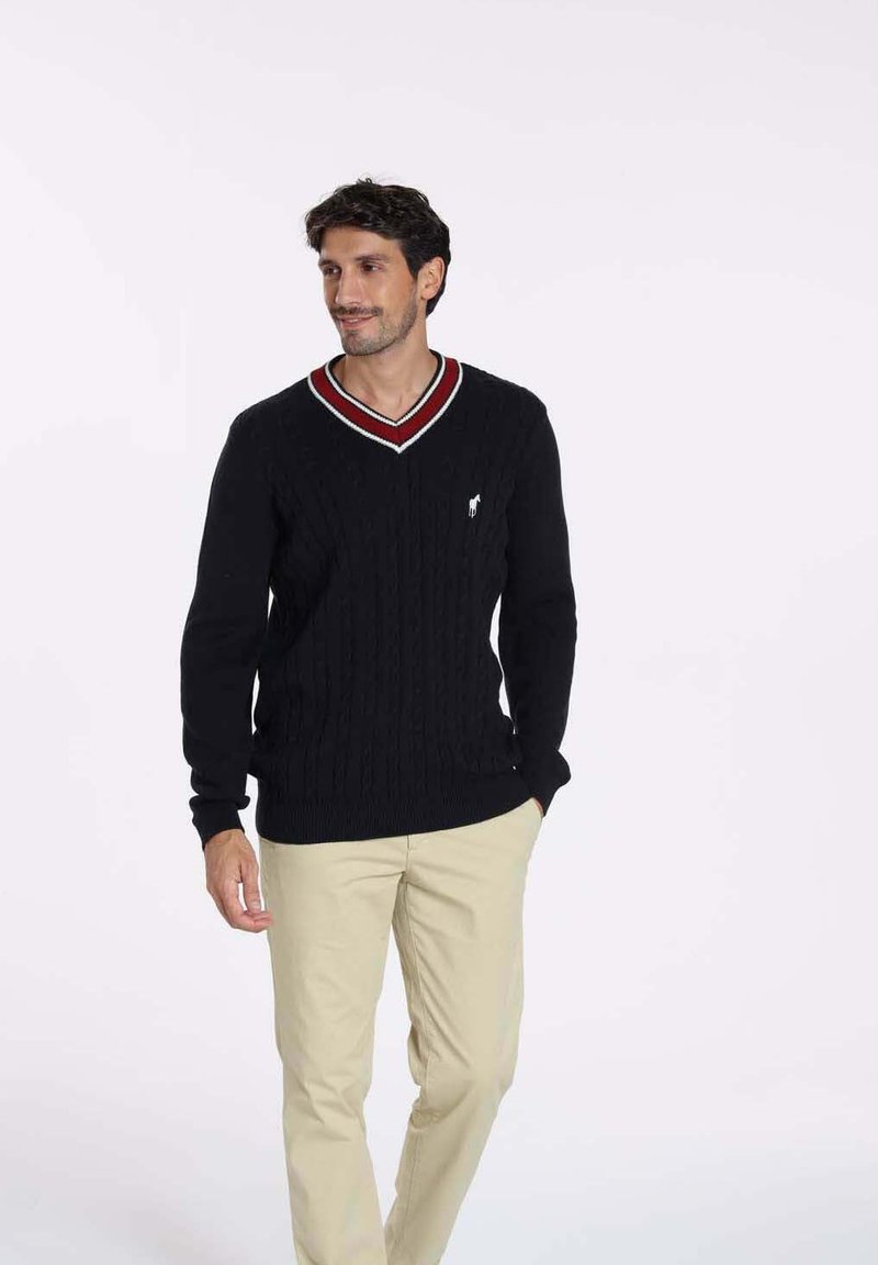 Pull en maille noir à col en V, avec des accents rayés rouges et blancs. Le design comprend un petit logo sur la poitrine.