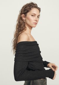 Schwarzes Off-Shoulder-Oberteil mit langen Ärmeln, aus einem strukturierten Strickstoff mit subtilen metallischen Fäden. Figurbetonte Silhouette mit gerolltem Ausschnitt.