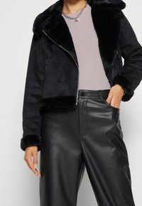 Svart fuskmockajacka med mjuk pälskrage och manschetter, dragkedjestängning, matchad med högmidjade svarta läderbyxor. Avslappnad, modern design.