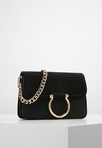 Borsa in suède e pelle nera con una tracolla in catena dorata e dettaglio hardware circolare. Presenta una chiusura a patta e una finitura testurizzata.