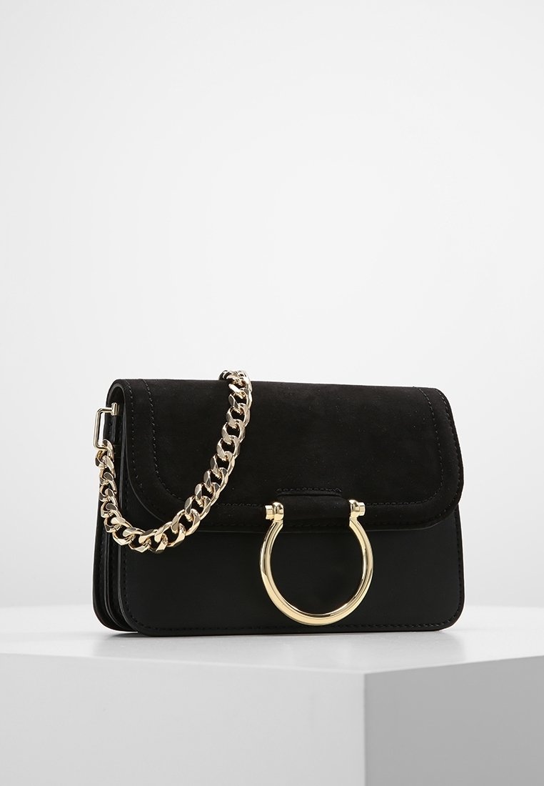 Borsa in suède e pelle nera con una tracolla in catena dorata e dettaglio hardware circolare. Presenta una chiusura a patta e una finitura testurizzata.