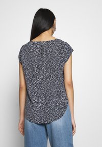 Blusa navy con piccolo motivo floreale bianco e azzurro, scollatura rotonda, maniche a cappuccio e dettaglio con zip sul retro. Tessuto morbido e leggero.