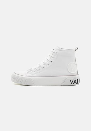 Witte hoge sneaker met veters, een dikke zool met geperste patronen en de tekst "VAL", en een ronde logopatch aan de zijkant.