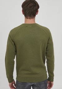 Felpa verde oliva con colletto a giro e maniche raglan. Tessuto morbido in misto cotone. Polsini e orlo a coste, cuciture minimali visibili.
