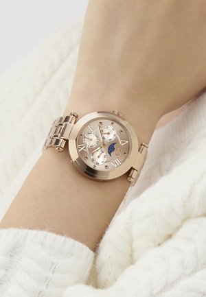 Rožinės aukso laikrodis ant riešo, su tekstūruotu ciferblatu, datų žymėjimais, trimis subciferblatais ir mėlyna mėnulio fazių indikatorių. Metalinė apyrankė.