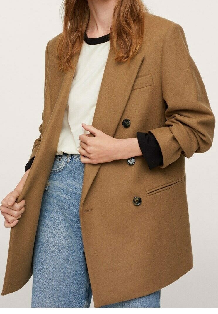 Brun dobbeltradet blazer med sorte knapper, skræddersyet pasform, blød tekstur og oprullede ærmer, båret over en hvid skjorte og blå jeans.