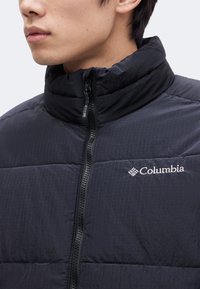 Νέος άνθρωπος που φοράει μαύρο μπουφάν Columbia με φερμουάρ μπροστά και ψηλό γιακά.
