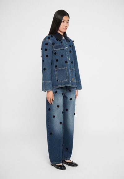 Denim jakna in široke jeanse z črnimi cvetličnimi aplikacijami, temnim ovratnikom in sprednjimi žepek. Prehod barv od svetlo do temno modre na jeansih.
