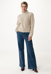Beige knitted turtleneck sweater with ribbed texture, paired with wide-leg blue jeans and burgundy heeled boots, set against a neutral background.
