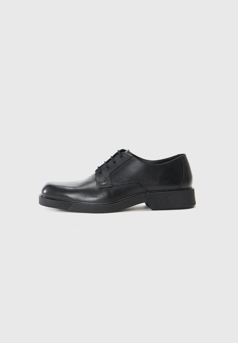 Zapato de vestir de cuero negro con punta redondeada, diseño con cordones y tacón bajo. Textura suave y perfil minimalista.