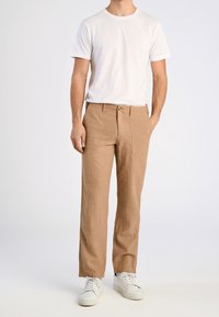 Ljusbruna linbyxor med en strukturerad finish, med framknäppning och sidofickor, tillsammans med en enkel vit t-shirt.