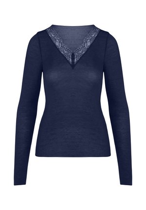 Vrouw met blond gevlochten knotje, gekleed in een marineblauwe top met lange mouwen en marineblauw ondergoed, strekt haar armen boven haar hoofd uit, met de rug naar de kijker tegen een effen achtergrond.